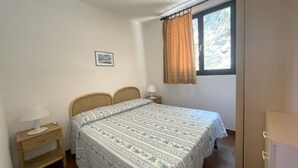 Une chambre à coucher avec un lit, des tables de chevet, une fenêtre avec des rideaux et un tableau accroché au mur.