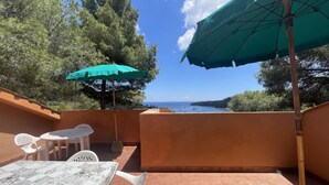 Une terrasse avec une table et des chaises, un parasol vert et une vue sur la mer.