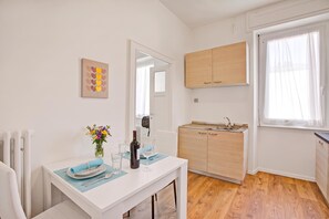 A compact kitchen with wooden cabinets, a dining area with a table set for two, and a window with sheer curtains.