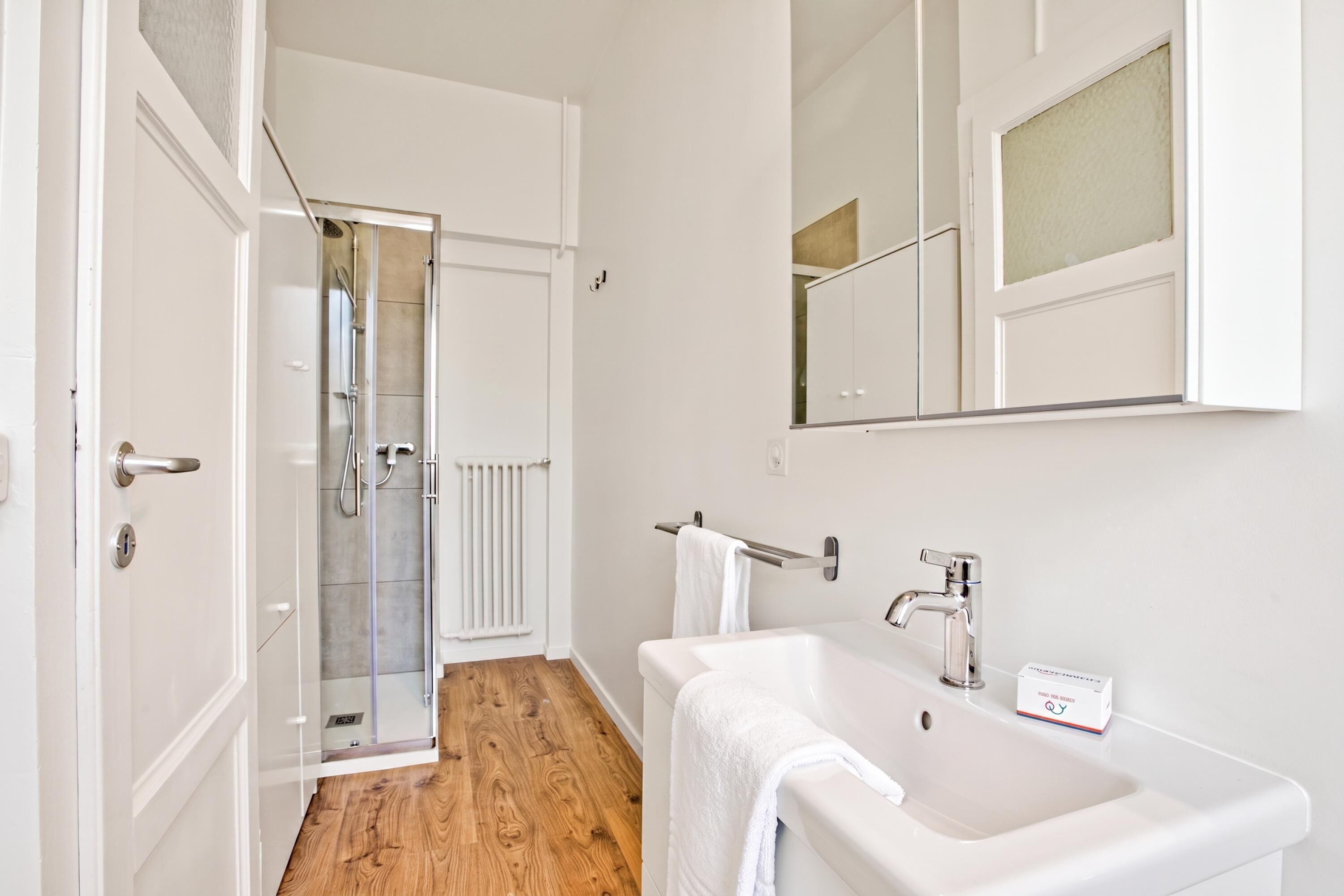 A modern bathroom with a glass shower enclosure, a white sink, and a mirror above the sink.