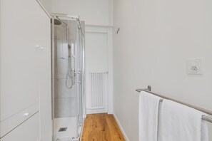 Un baño estrecho con ducha, un radiador blanco y un perchero.