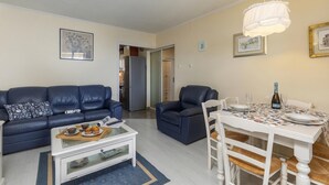 Un salon avec un canapé, une table à manger dressée pour deux personnes et un réfrigérateur en arrière-plan.