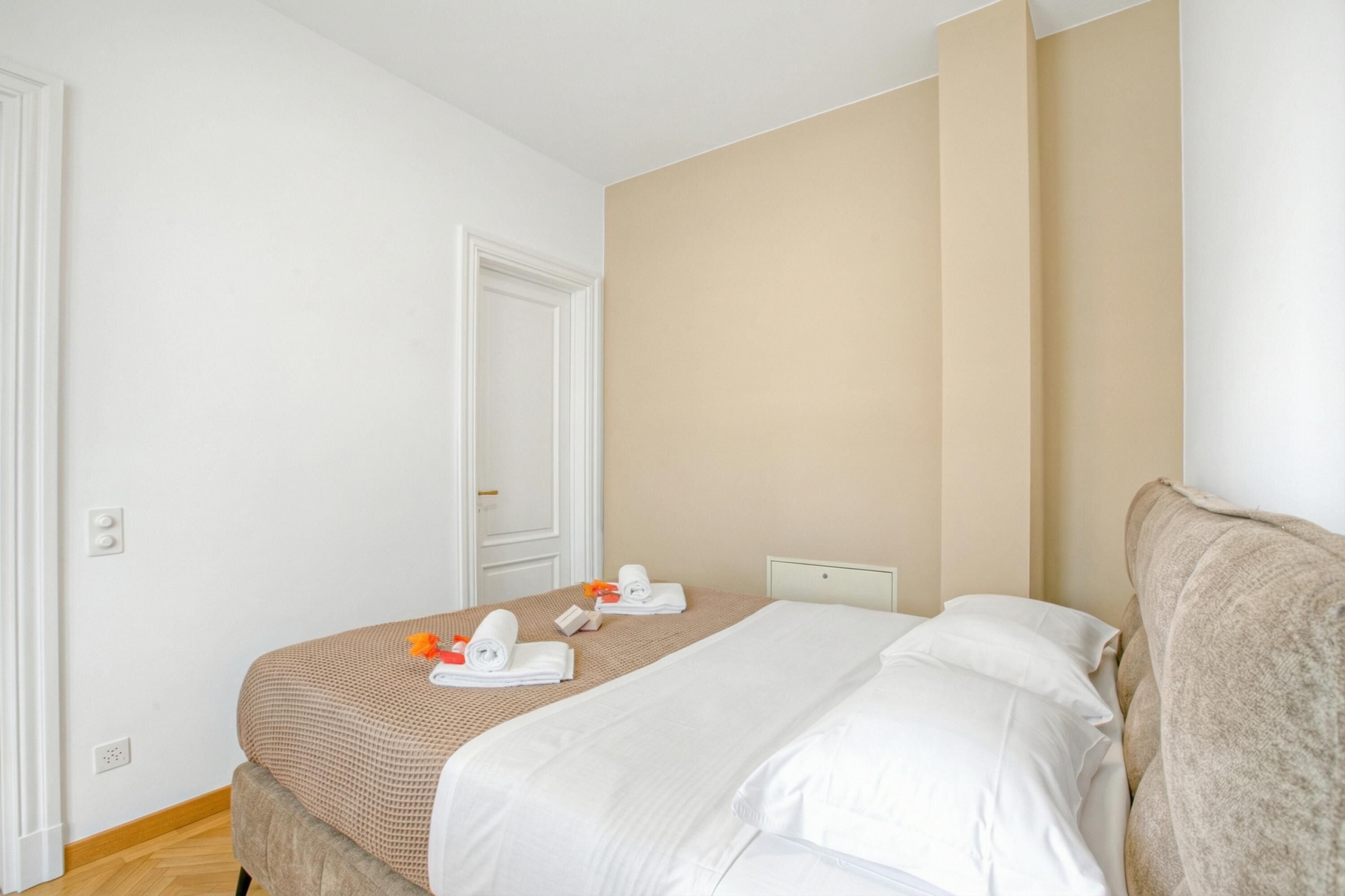A hotel room with a bed, a bedside table, a door, and a wall.