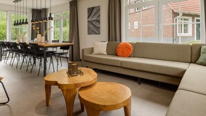 Ein modernes Wohnzimmer mit einer Couch, einem Esstisch mit Stühlen und einem großen Fenster mit Blick auf ein Backsteingebäude.