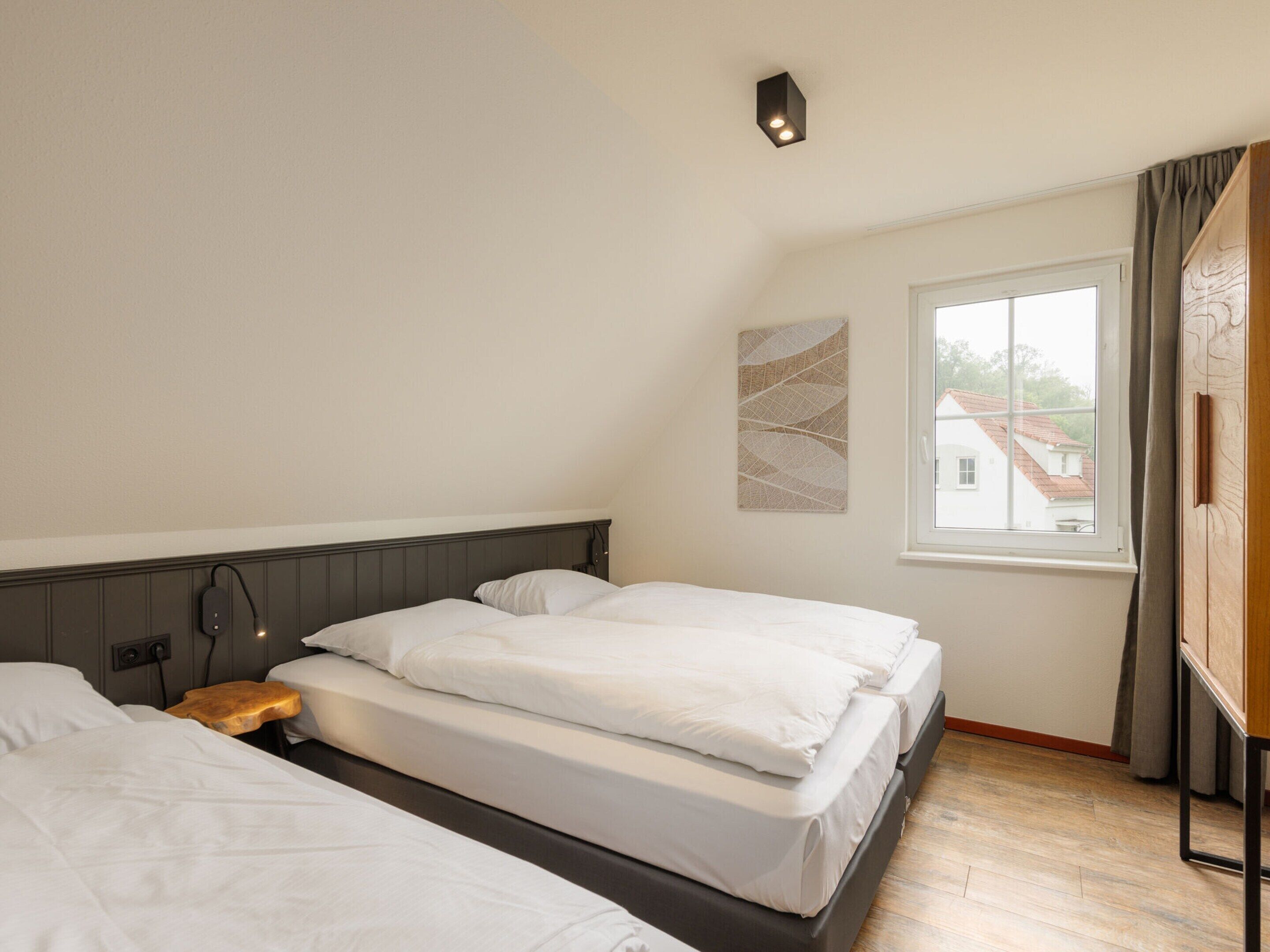 A bedroom with two beds, a window with curtains, and a wall-mounted light fixture.