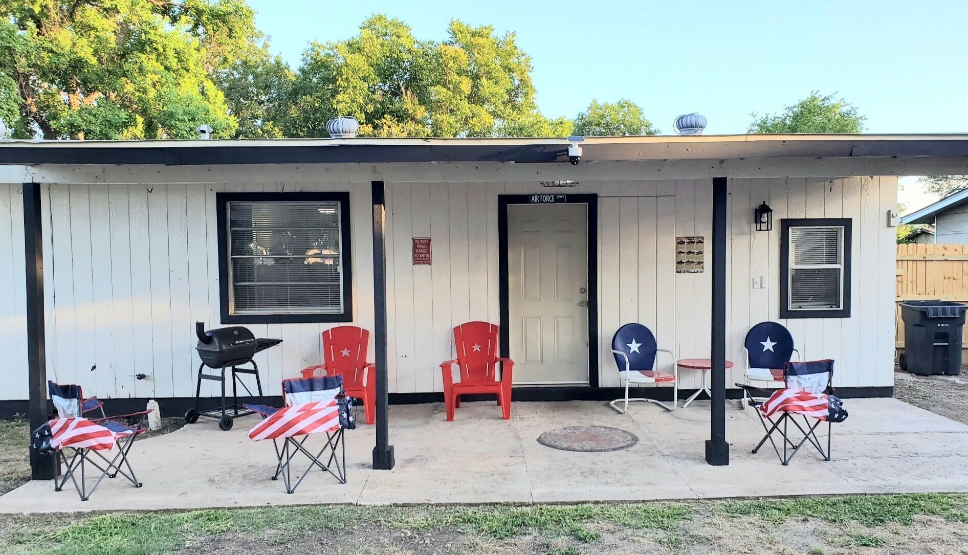 Ein kleines Gebäude mit einer Veranda, einer Tür mit der Aufschrift "Air Force Way" und mehreren Stühlen mit US-amerikanischen Flaggen.