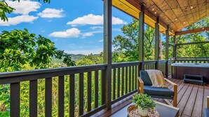 Una terraza de madera con vistas a colinas verdes, un jacuzzi y una mesa con una planta.