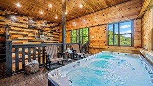 Interior de una cabaña de madera con jacuzzi, terraza de madera y vistas al exterior.