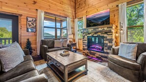 Interior acogedor de una cabaña de madera con chimenea, sofás de cuero y un amplio ventanal con vistas panorámicas.