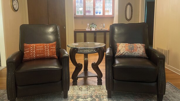 Two leather armchairs with patterned cushions, a small glass table, and a decorative cabinet with glass doors in the background. - Spacious home near medical / college (Tyler)