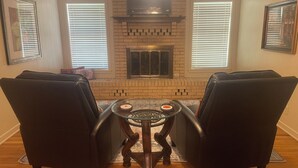 A living room with a brick fireplace, two black leather chairs, a glass coffee table, and a television mounted above the fireplace. - Spacious home near medical / college (Tyler)