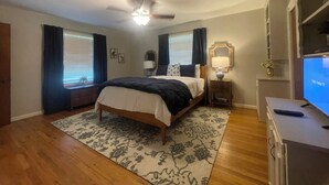A bedroom with a bed, a ceiling fan, a nightstand with a lamp, a TV, and a window with curtains. - Spacious home near medical / college (Tyler)