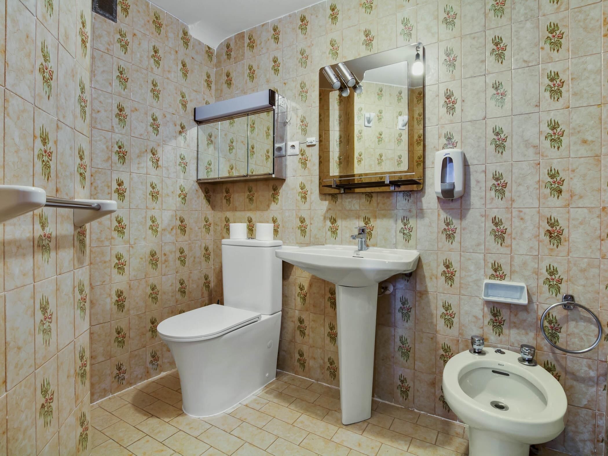 Une salle de bain comprenant des toilettes, un lavabo, un bidet et un miroir au-dessus du lavabo.