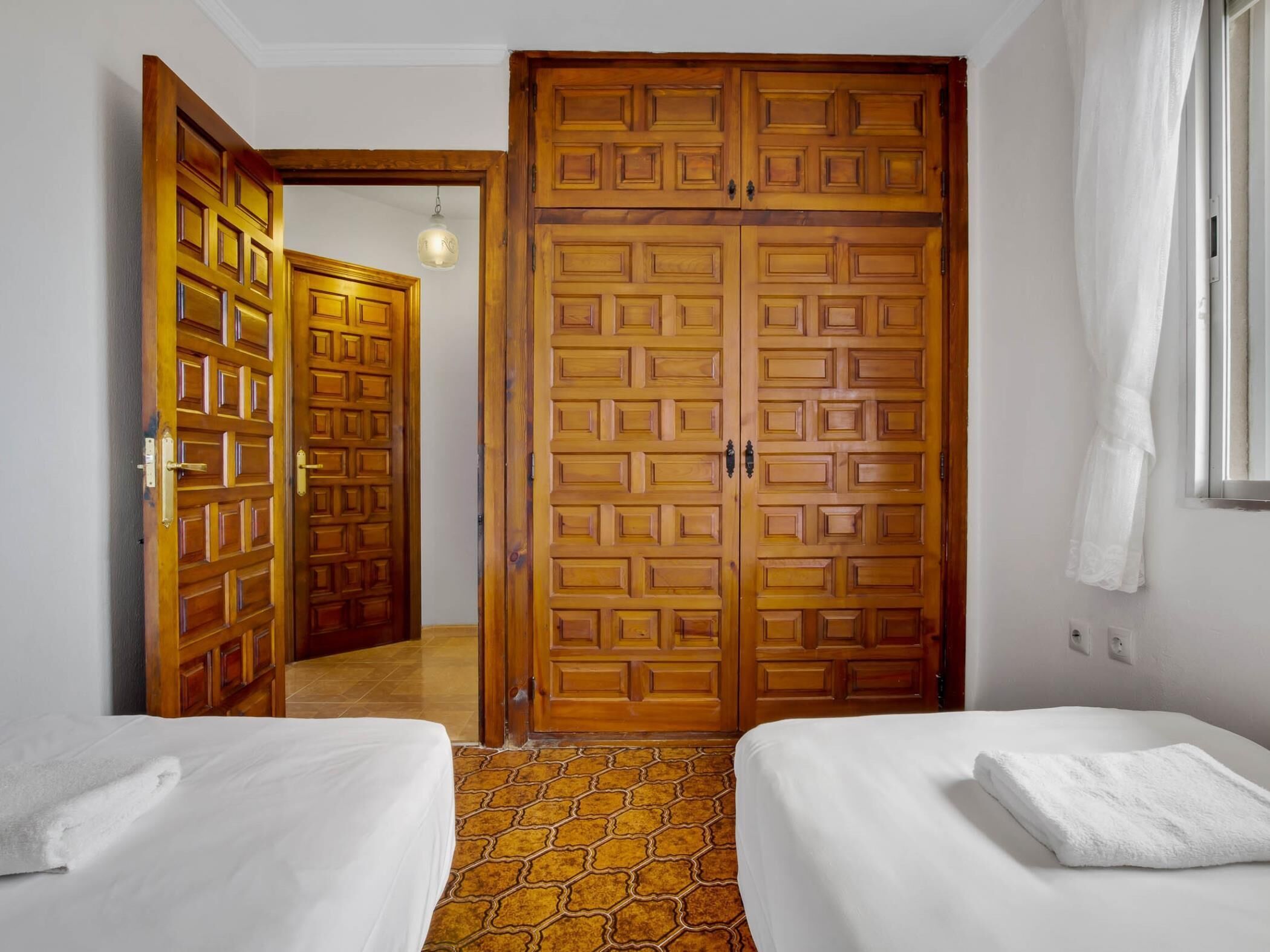 A hotel room with two beds, a large wooden wardrobe, and a tiled floor.
