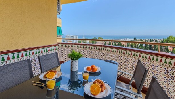 A dining table with breakfast items, a view of the sea, and a tiled balcony wall. - El Rocio 7E1 - Terrace, Swimming Pool, Sea Views (Torremolinos)