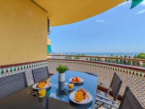 A dining table with breakfast items, a view of the sea, and a tiled balcony wall.