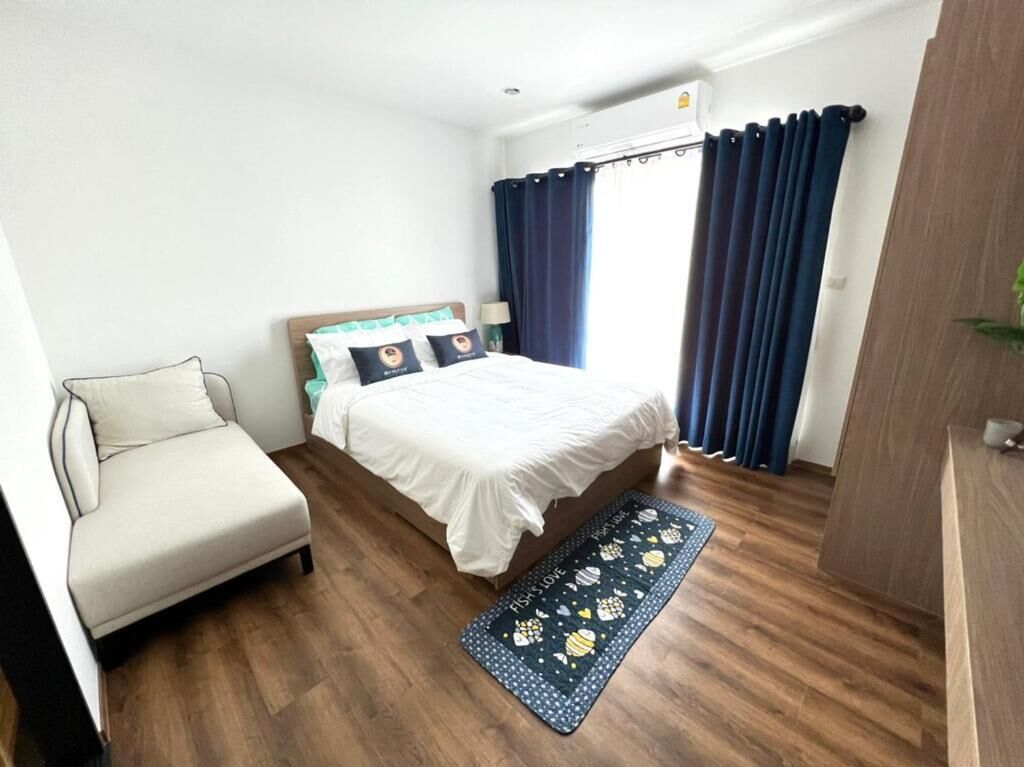 Un dormitorio con una cama, una silla, un ventanal con cortinas y suelo de madera.