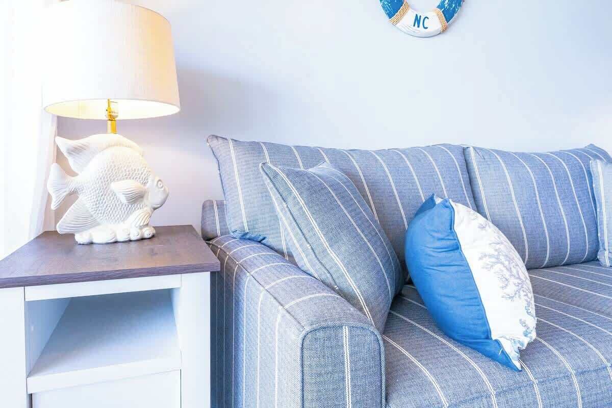 Un divano a righe blu con un tavolino bianco e una lampada a forma di pesce.