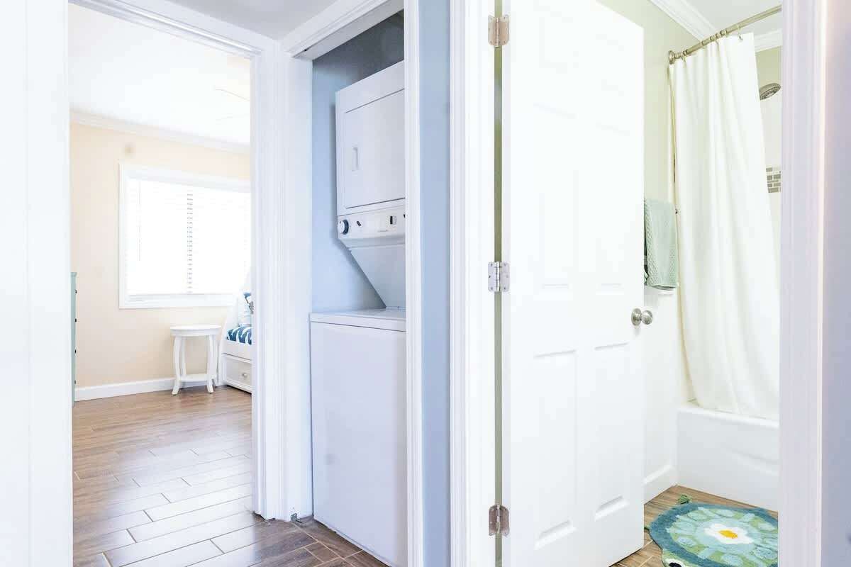 A laundry room with a washing machine and dryer, a small table with a chair, and a shower area with a curtain.
