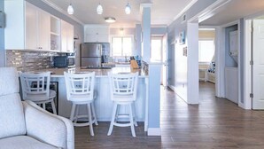 A modern kitchen with white cabinetry, a central island with bar stools, stainless steel appliances, and pendant lighting.
