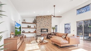 A modern living room with a stone accent wall, a fireplace, a leather sofa, and a large TV. - Luxe Haven (Moama)