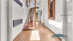 A hallway with a wooden staircase, white walls, and a wooden floor. - Luxe Haven (Moama)