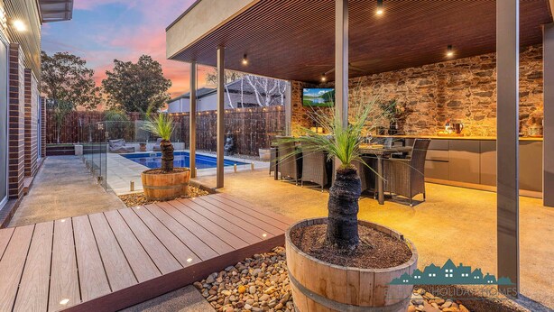 A modern outdoor patio with a pool, wooden planters, and a stone wall. - Luxe Haven (Moama)
