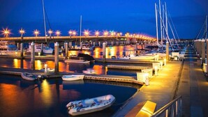 A marina at dusk with boats docked, a bridge in the background, and lights illuminating the area.