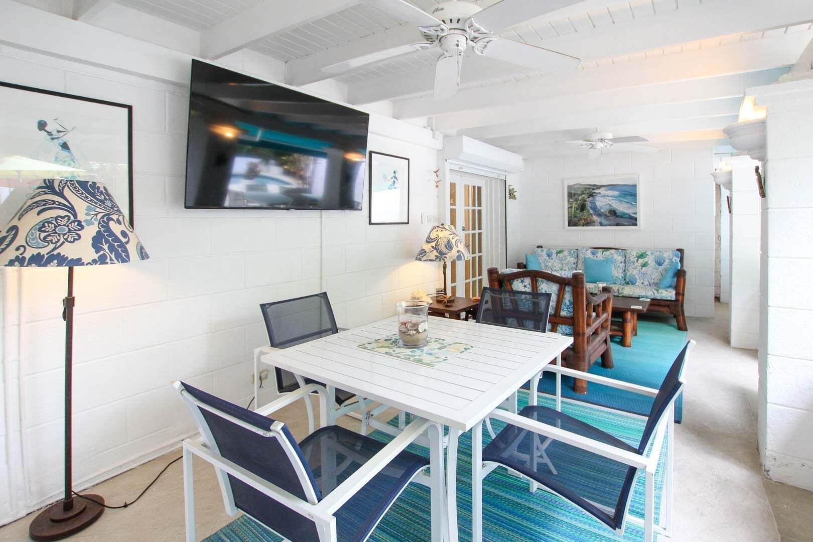 Un coin repas avec une table blanche, des chaises bleues, un téléviseur fixé au mur et un tableau accroché au mur.