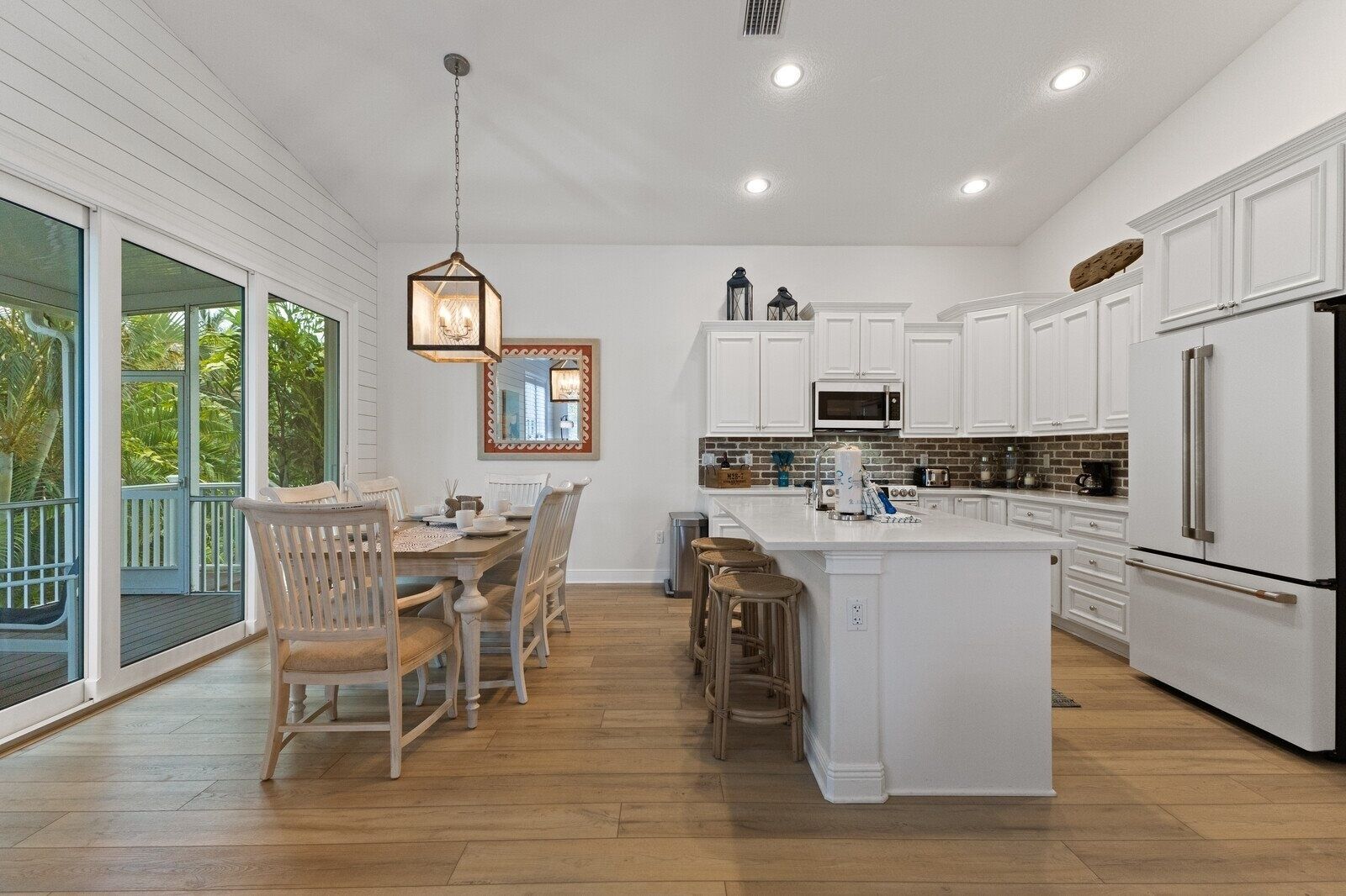 A modern kitchen with white cabinetry, a large island, and a dining area with wooden chairs.