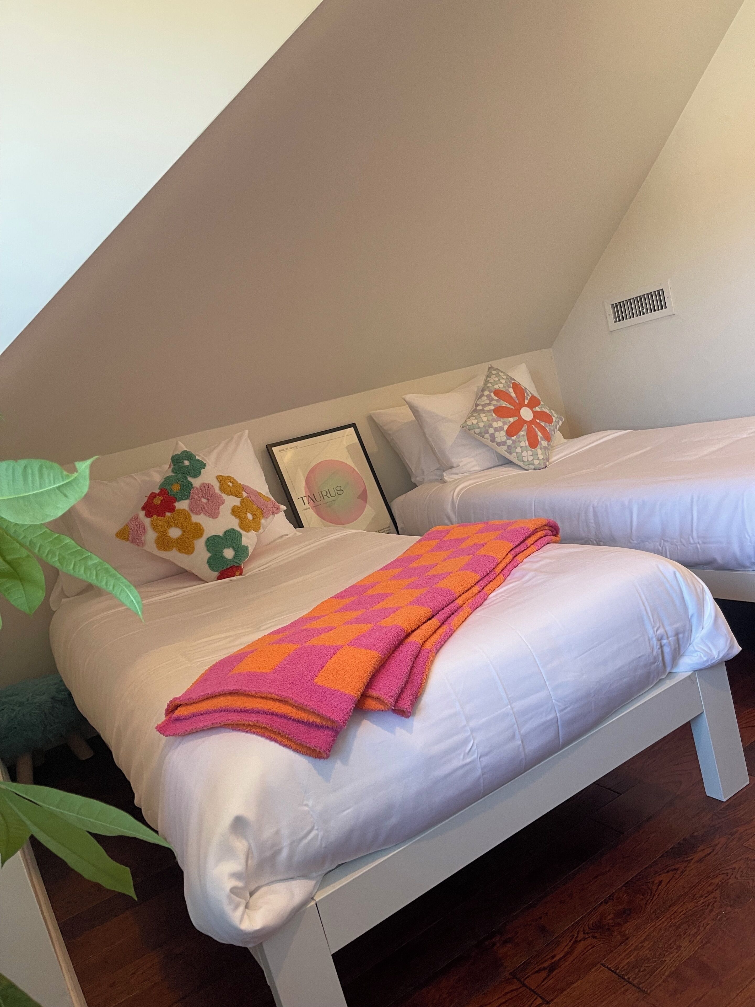 A bedroom with two single beds, white bedding, colorful pillows, and a framed picture on the wall.