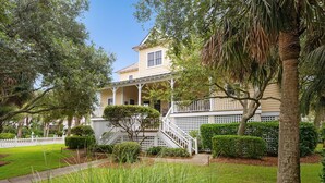 A two-story house with a porch, surrounded by well-maintained lawns and trees. - Screened Porches, Decks, Rockers, Hammocks And An Upstairs Balcony With Ocean Views 5 Bedroom Home by Peace Vacations (Georgetown)