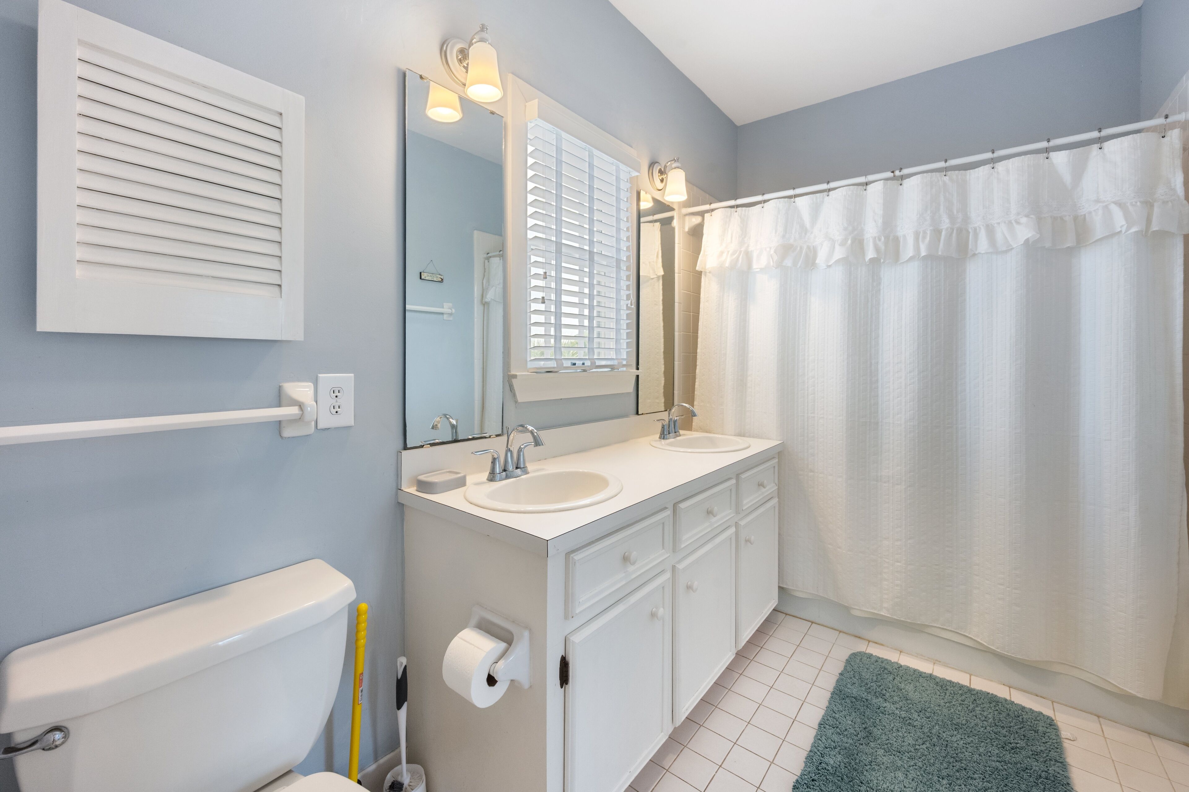 A bathroom with a toilet, two sinks, a mirror, a towel rack, and a shower curtain.
