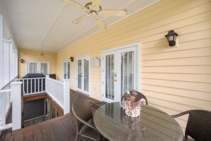 A covered patio with a glass table and wicker chairs, a ceiling fan, and a view of the house through white shutters. - Screened Porches, Decks, Rockers, Hammocks And An Upstairs Balcony With Ocean Views 5 Bedroom Home by Peace Vacations (Georgetown)