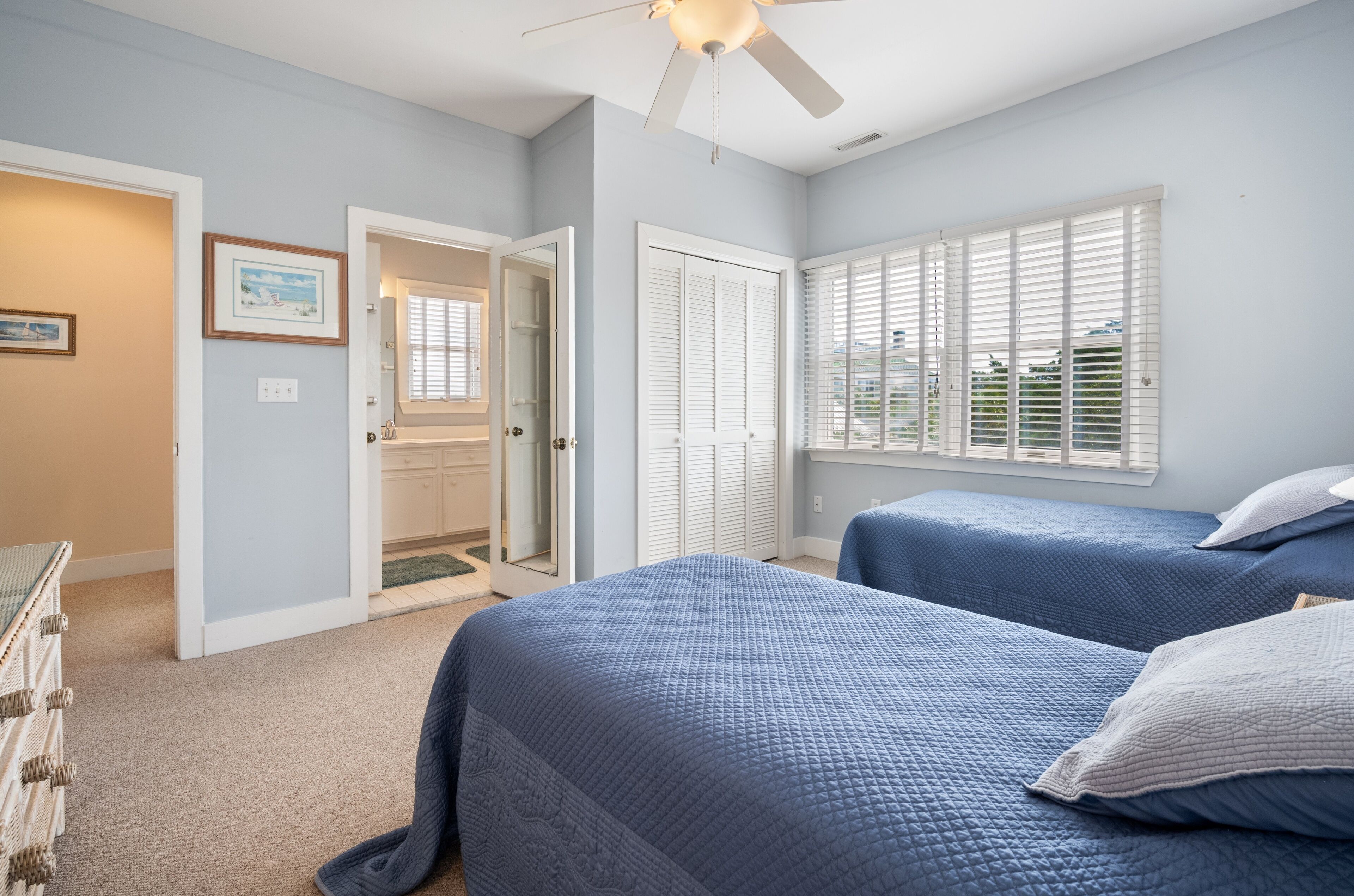 A bedroom with two beds, a ceiling fan, and a door leading to a bathroom.