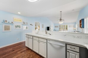 A kitchen with a white countertop, a dishwasher, and a sink. There are framed pictures on the wall and a ceiling fan. - True Blue On 10th Hole, A Perfect Retreat For Golf Enthusiasts And Those Seeking A Relaxing Getaway 3 Bedroom Condo by Peace Vacations (Pawleys Island)