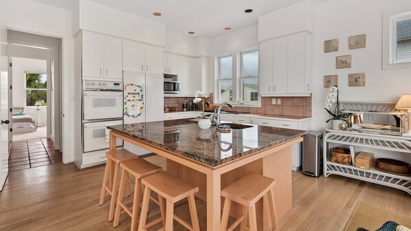 A spacious kitchen with white cabinetry, a granite island with bar stools, and a view of the outdoors.