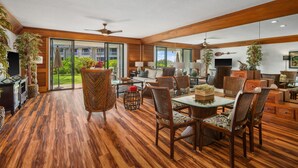 A spacious living area with a wooden floor, large windows, and a dining table with chairs.