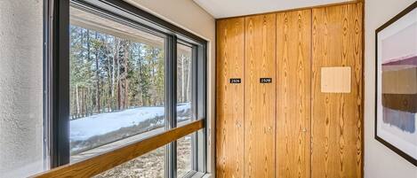 A corner room with a large window, a wooden door with two labels, and a carpeted floor.