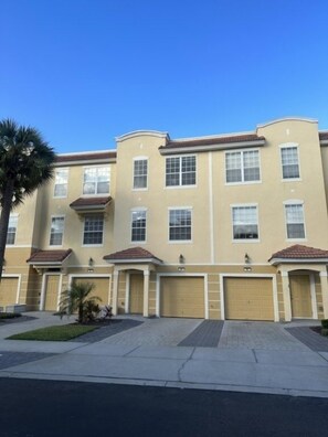 Un edificio residencial de varios pisos con fachada color beige, varios portones de garaje y un camino de entrada pavimentado.