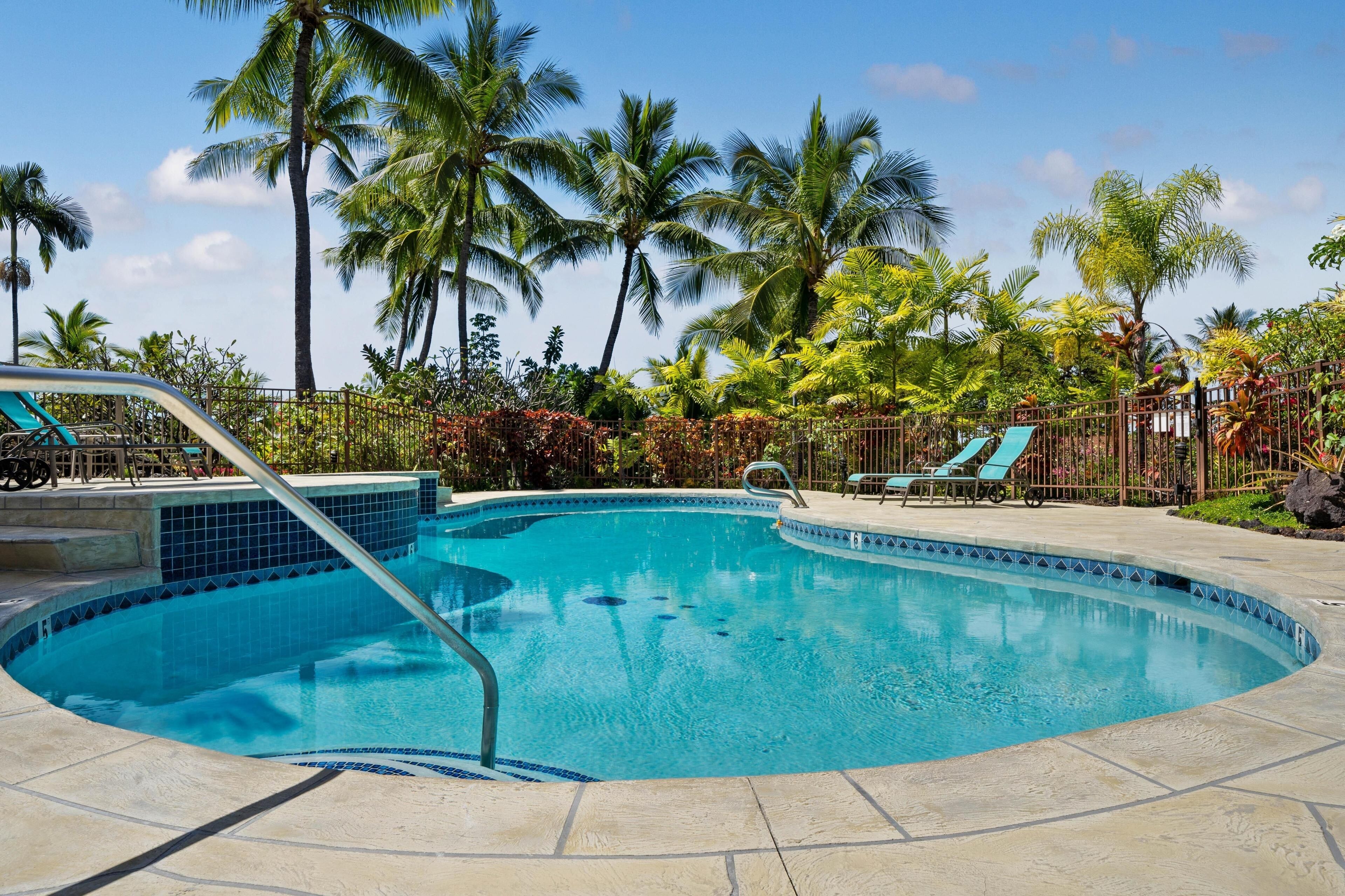 Une piscine dont le bord est recouvert de carrelage, entourée de palmiers et de chaises longues.