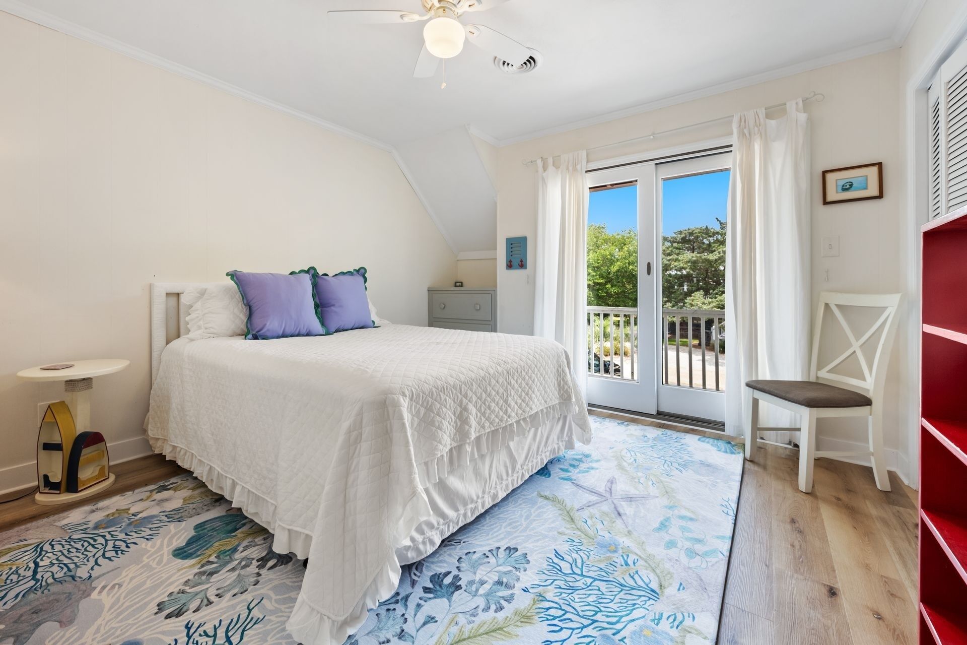 A bedroom with a bed, a nightstand, a chair, a window with a view, and a ceiling fan.