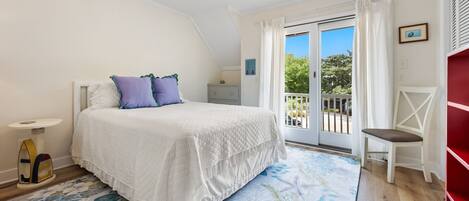 A bedroom with a bed, a nightstand, a chair, a window with a view, and a ceiling fan.