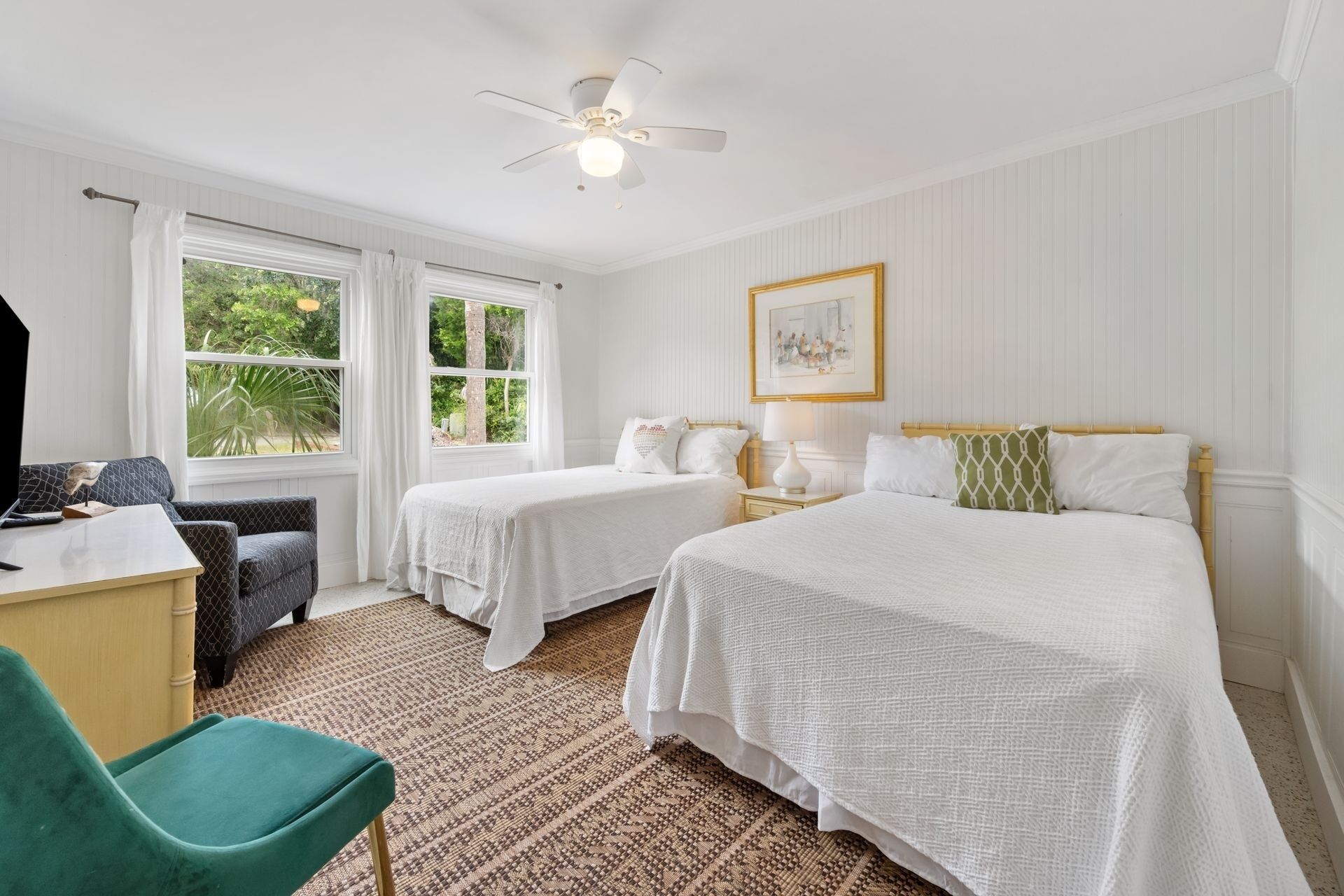 A hotel room with two beds, a desk, a chair, and a ceiling fan.