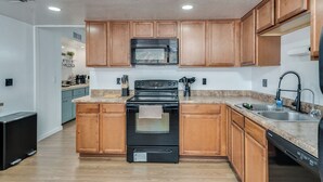 Cucina con mobili in legno, piano cottura nero, forno a microonde ed elettrodomestici inclusa la lavastoviglie.