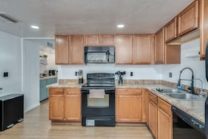 A kitchen with wooden cabinets, a black stove, a microwave, and a dishwasher.