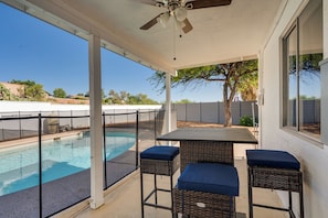 A covered patio with a pool, two wicker chairs with cushions, and a table.