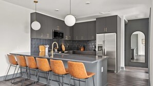 Une cuisine moderne dotée d’un îlot central, de tabourets de bar, de luminaires suspendus et d’appareils électroménagers en acier inoxydable.