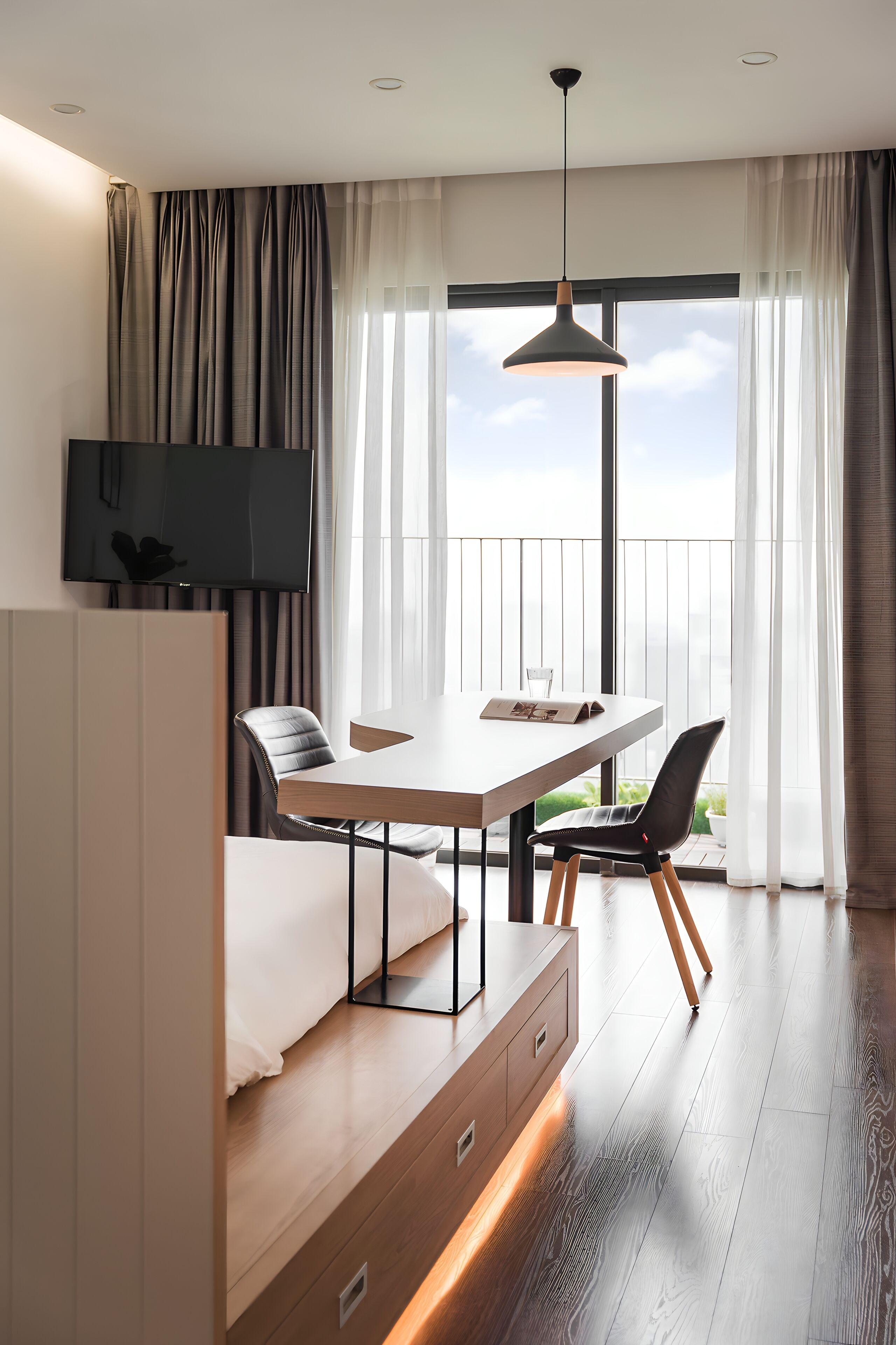 A modern hotel room with a convertible bed, a dining table, and a TV.