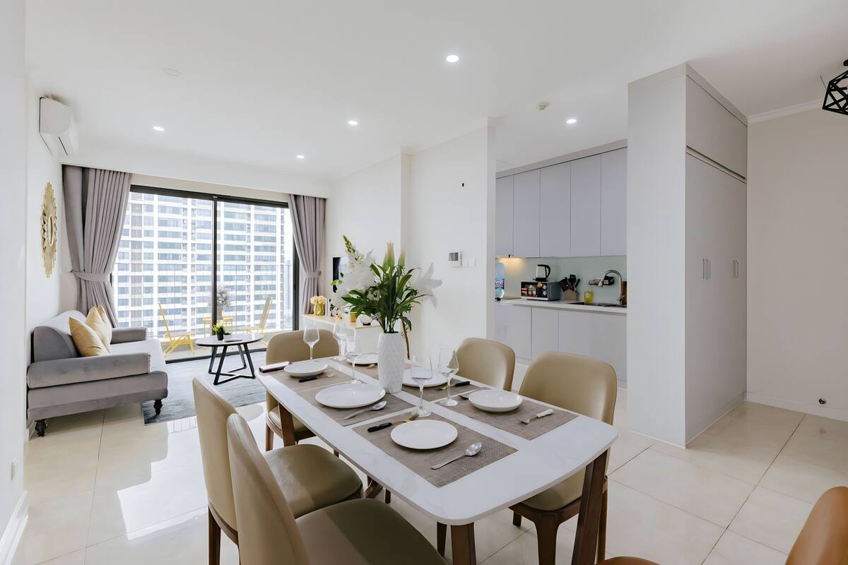Una sala moderna con comedor, un sofá, una mesa de centro y vistas de la ciudad a través de grandes ventanales.